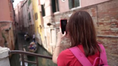 Venedik. Bir turist telefonuyla dar bir kanalda yelken açan tekneleri filme alıyor..