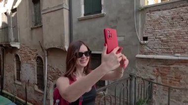 Venedik. Bir turist telefonuyla dar bir kanalın arka planında kendi fotoğrafını çeker..