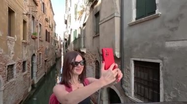 Venedik. Bir turist telefonuyla dar bir kanalın arka planında kendi fotoğrafını çeker..