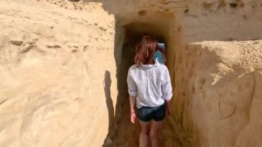 Bir kadın kayalık bir tünelden geçer ve denize çıkar..