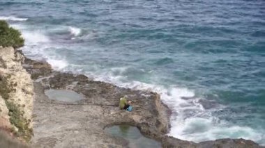 - Lecce. İtalya. 14 Ekim 2023. Balıkçı. Kayaların ve denizin güzel manzarasıyla balık tutan bir adam..