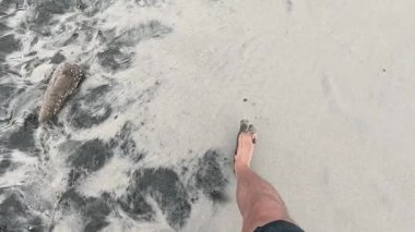 Sahilde ıslak kumda yürüyen erkeklerin ayakları..