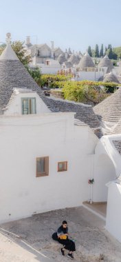 Bir kadın evin girişinin yanında oturuyor. Apulia 'daki beyaz evler.