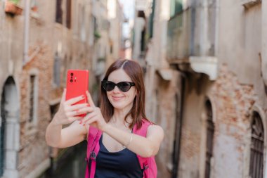 Venedik. Bir turist telefonuyla dar bir kanalın arka planında kendi fotoğrafını çeker..