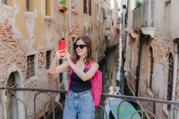 Venedik. Bir turist telefonuyla dar bir kanalın arka planında kendi fotoğrafını çeker..