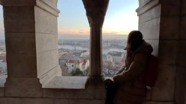 Pencerede bir kadın oturuyor. Şafak Bir kadın izleme platformunda bir caddede duruyor ve şehre bakıyor..