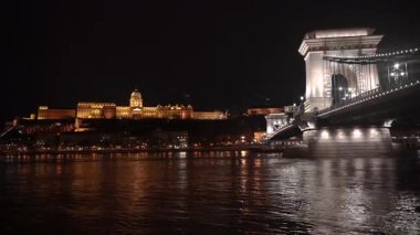 Gece şehri. Aydınlanmış bir binanın arka planına karşı bir eğlence gemisi köprünün altından geçiyor..