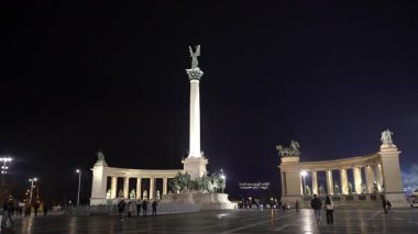 Gece şehri. Meydanda yürüyen insanlar.