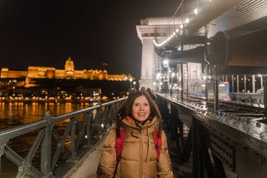 Bir kadın bir gece şehrinin arka planına karşı köprüden geçiyor..