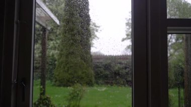Yağmur. Pencerenin dışındaki yağmur damlaları yeşil çimlerin arka planına karşı.