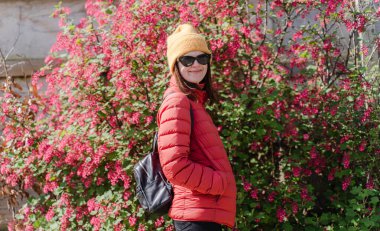 Güneşli bir günde, çiçek açan bir çalılığın arka planına gülümseyen bir kadın..