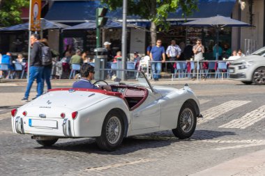 Kırmızı çatılı beyaz spor araba caddede ilerliyor.