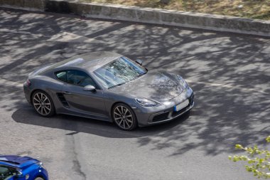 Gri Porsche 718 baharda bir kır yolunda gidiyor.
