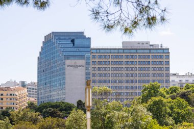 Lizbon, Portekiz 'de yeşil ağaçların üzerinde yükselen modern otelin arka planında parlak mavi bir gökyüzü var.