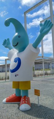 Dev maskot, üzerinde fotokopi alanı olan bir tişört giyiyor. Kutlama için mavi gökyüzünün altında kollarını kaldırıyor.