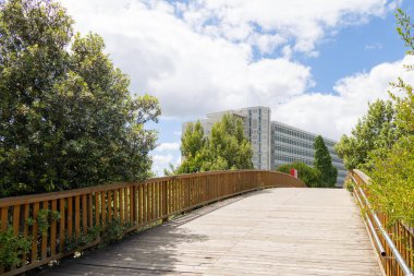 Tahta bisiklet köprüsü, parlak mavi gökyüzü ve Lizbon, Portekiz 'de beyaz bulutları olan modern bir ofis binasına açılıyor.