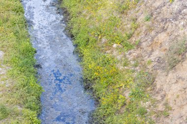 Kirlenmiş endüstriyel su küçük bir kanaldan akıyor ve çevreyi kirletiyor.