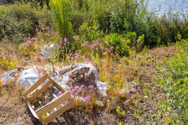 Ahşap sandık ve inşaat enkazı kır çiçeklerinin arasında terk edilmiş vaziyetteydi ve doğal ortamlardaki kirlilik sorununu vurguluyordu.