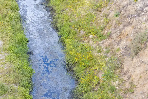 Kirlenmiş endüstriyel su küçük bir kanaldan akıyor ve çevreyi kirletiyor.