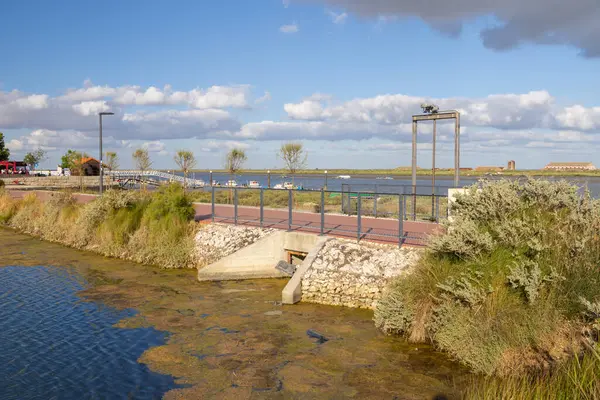 Mavi gökyüzü ve beyaz bulutlarla güneşli bir günde nehir parkındaki gelgit tanklarına akan su.