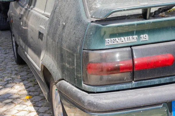 Kirli, yeşil bir Renault 19 rti 'yi kaldırım taşı sokağına park edip yaşını ve giyim tarzını gösteriyor.
