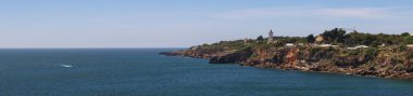 Cascais, Portekiz 'de güneşli bir günde kayalık bir sahil şeridinde duran bir deniz fenerinin panoramik görüntüsü