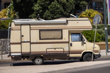 Eski ve kirli bir karavan, Avrupa 'da bir caddede, ön lastiği patlamış bir şekilde yasa dışı park halinde.