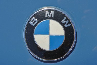 Mavi bir yüzeyde güneş ışığında parlayan bir BMW logosunun yakın çekimi.