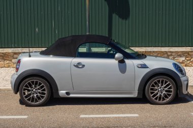 Açık çatılı gümüş rengi Cabrio Cooper, güneşli bir yaz gününde yeşil bir duvarın yanına park eder.