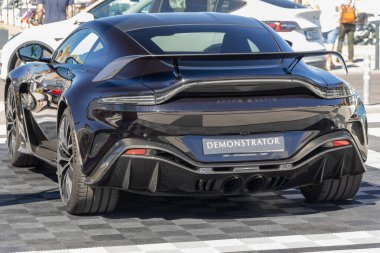 Siyah bir Aston Martin Vantage Coupe göstericisinin arkası kareli bir yüzeye park edilmiş.