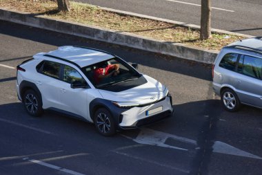 Adam güneşli bir günde beyaz bir Toyota bz4x elektrikli araba kullanıyor, sürdürülebilir ulaşım için modern otomotiv teknolojisi sergiliyor.