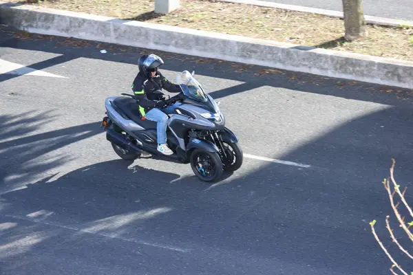 Kask takan adam güneşli bir günde Jamaika tricity 3 tekerlekli scooter sürüyor.