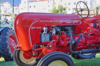 Kırmızı Porsche dizel ap22 traktörü büyük sarı tekerlekleri olan çimenli bir alanda park halinde.