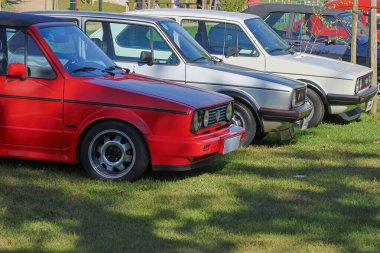 Üstü açık kırmızı Volkswagen golf gti diğer arabalarla birlikte bir araba fuarında çimlerin üzerine park edilmiştir.