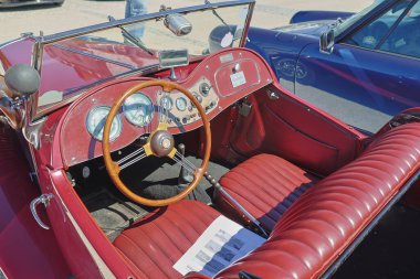 Üstü açılır klasik bir İngiliz arabasının iç görüntüsü. Gösterge paneli, direksiyon simidi ve kırmızı deri koltuklar.
