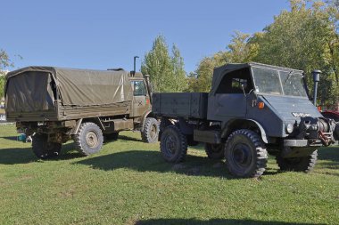 Bir zamanlar Portekiz ordusu tarafından kullanılan iki klasik unimog kamyonu, çimenli bir alana park edilmiş, güçlü tasarımlarını ve tarihsel önemlerini sergiliyorlar.