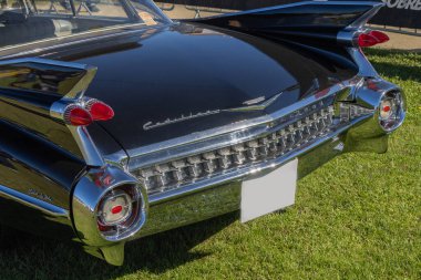 Klasik Cadillac coupe deville çimlerin üzerine park edilmiş, ikonik kuyruk yüzgecini ve krom tamponunu sergiliyor