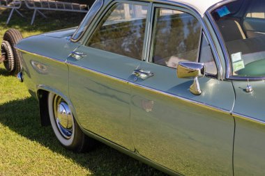 Turkuaz Chevrolet Corvair, klasik bir araba fuarında güneşte parlıyor.