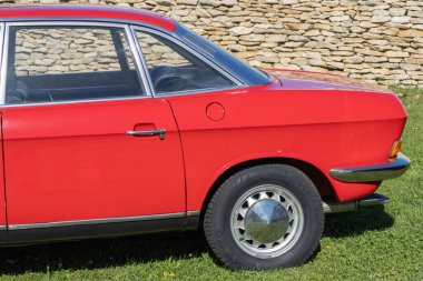 Taş duvarın önündeki çimlerin üzerine park edilmiş kırmızı Nsu Ro 80.