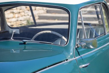 Güneş ışığı, Simon Aronde marka klasik bir arabanın turkuaz gövdesine yansıyor. Direksiyon simidi ön camdan görülebiliyor.
