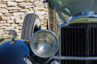 Taş bir duvarın önüne park edilmiş klasik bir otomobilin parlak krom farları.