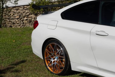 Modern beyaz BMW M4 otların üzerine park edilmiş, spor tasarımı ve lüks özellikleri sergileniyor.