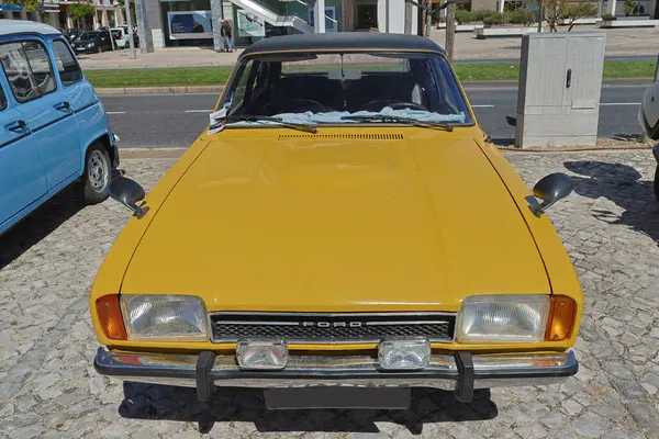 Sarı Ford Cortina bir kaldırım taşı caddesinde park halinde, klasik tasarımını sergiliyor.