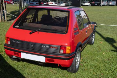 Kırmızı peugeot 205 Gti bir araba fuarında çimlerin üzerine park edilmiş.