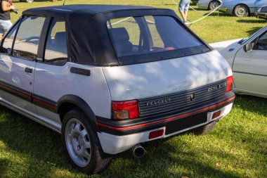 Beyaz peugeot 205 Cti Cabriolet bir araba fuarının çimlerine park edilmiş, arka ve sağ tarafını gösteriyor.