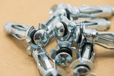 Vidalı birkaç yeni ve parlak metal alçıpan çapası kahverengi bir yüzey üzerinde duruyor.