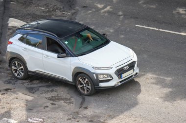Adam yolda beyaz bir hyundai Kona SUv kullanıyor.