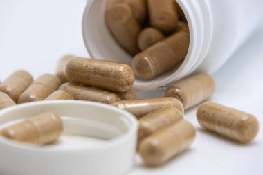 Bitkisel ilaç kapsülleri beyaz bir yüzeye dökülüyor.