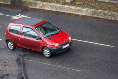 Kırmızı renault twingo, güneşli bir günde bir adam tarafından sürülüyor.