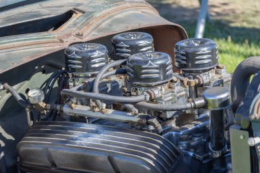 Dört karbüratörü olan güçlü özelleştirilmiş V8 motoru güneşte parlıyor ve mekanik detayları gösteriyor